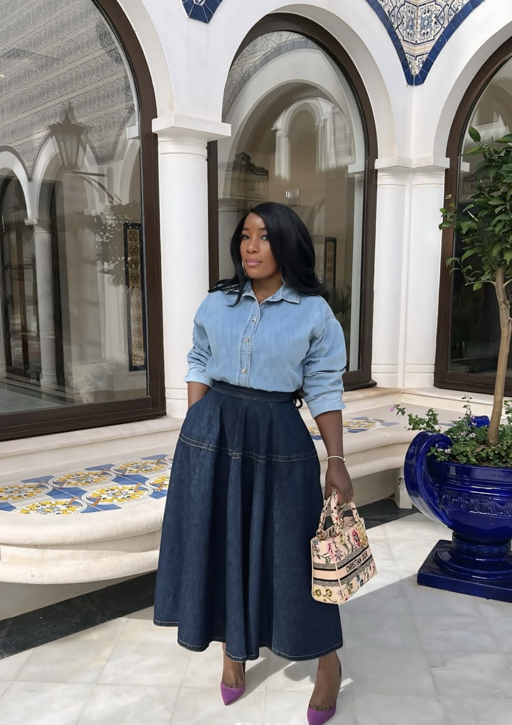 Woman wearing a dark denim A-line midi skirt with a tucked chambray shirt and purple pointed pumps