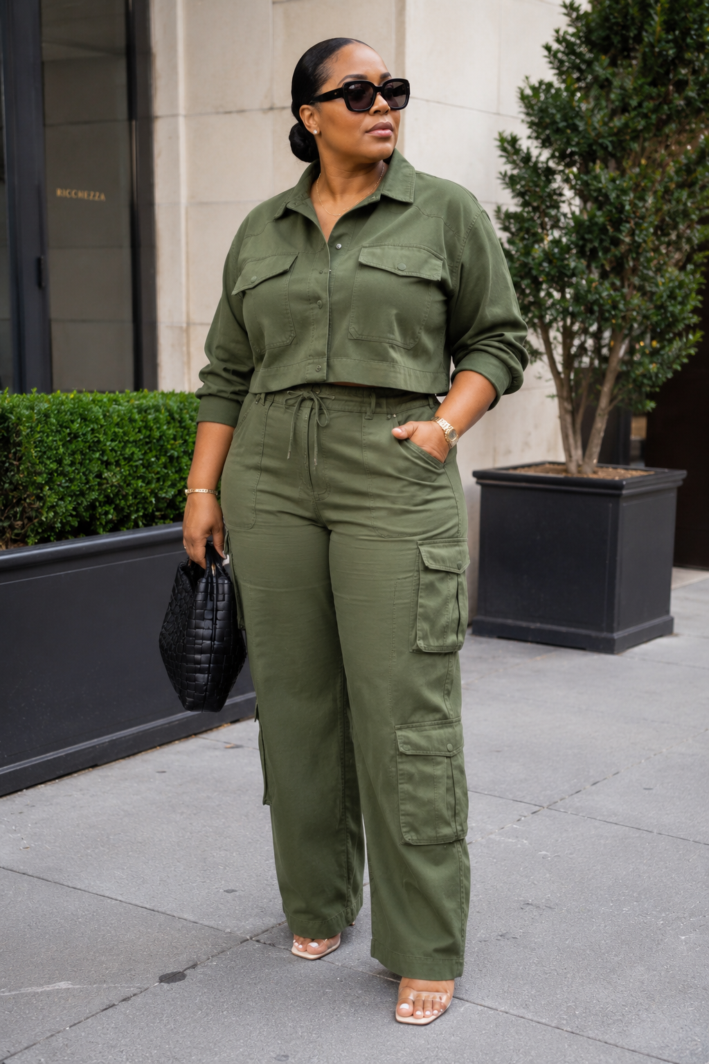 A person wearing a monochromatic olive green matching set featuring a long-sleeve button-down cargo shirt and wide-leg cargo pants, styled with a black quilted handbag and neutral-toned sandals.