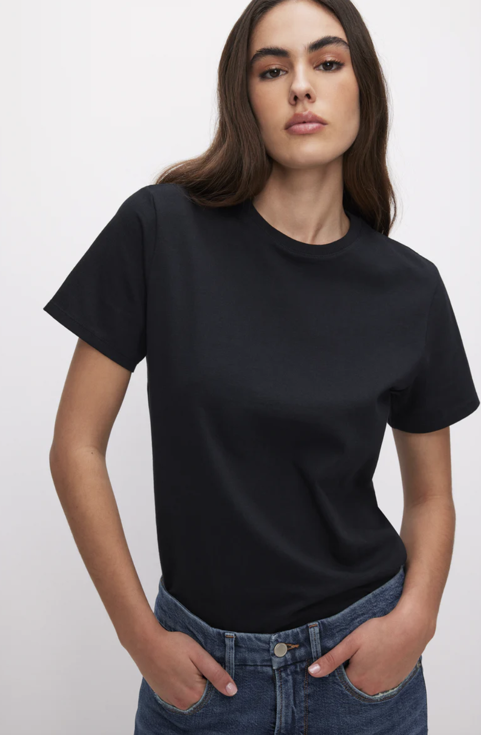 A close-up view of a person wearing a classic black short-sleeve crewneck t-shirt tucked into blue denim jeans.