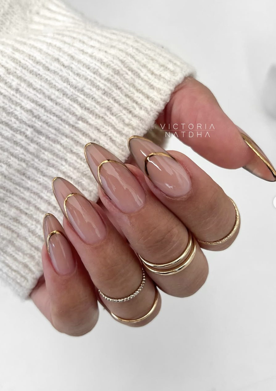 Long almond-shaped nails with a glossy nude base and a metallic gold chrome crescent line across the center, highlighting cute June nail ideas.
