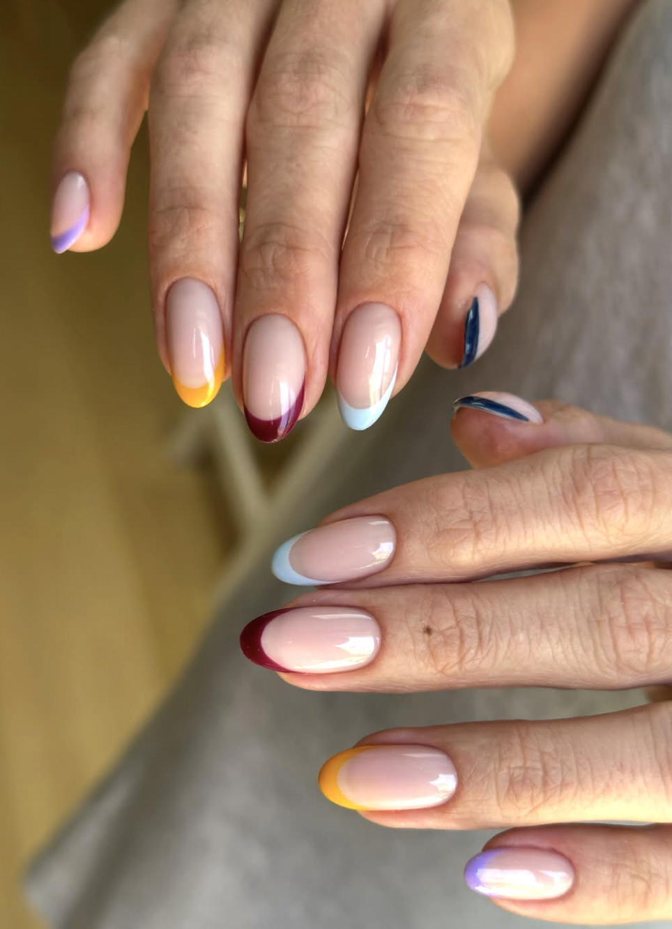 Close-up of a multi-colored micro French manicure on short nails featuring alternating fall shades on each tip including espresso, olive green, rust, burgundy, and navy over a sheer nude base.