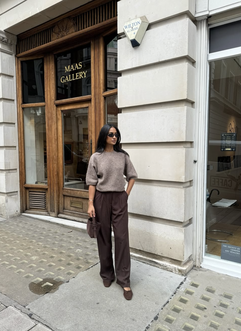 A woman wearing dark brown trousers paired with a tan sweater and matching brown ballet flats, demonstrating a tonal brown pants outfit idea.