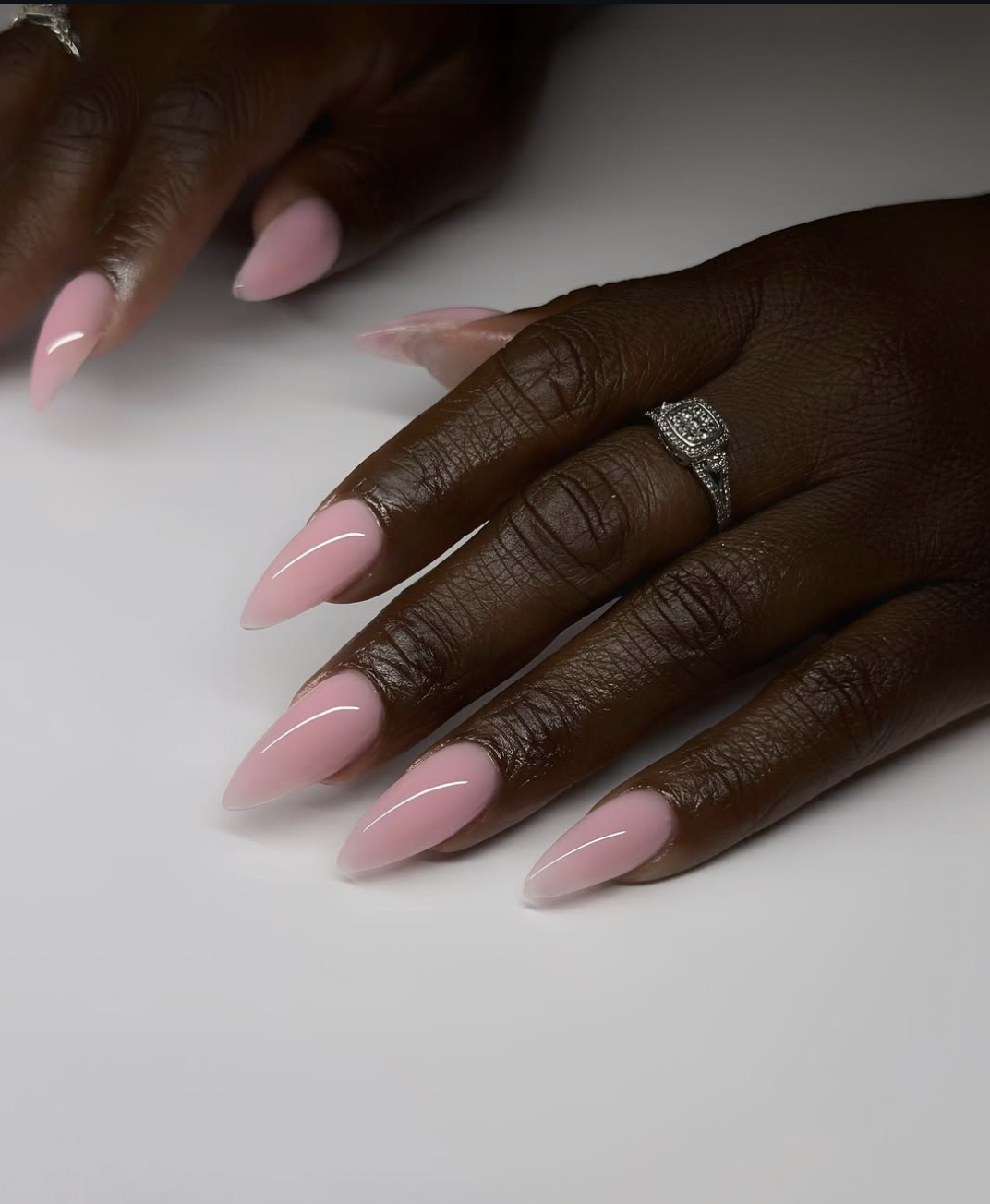 Long, almond-shaped nails showcasing a semi-sheer strawberry pink base coat with a high-shine iridescent pearl chrome glaze.