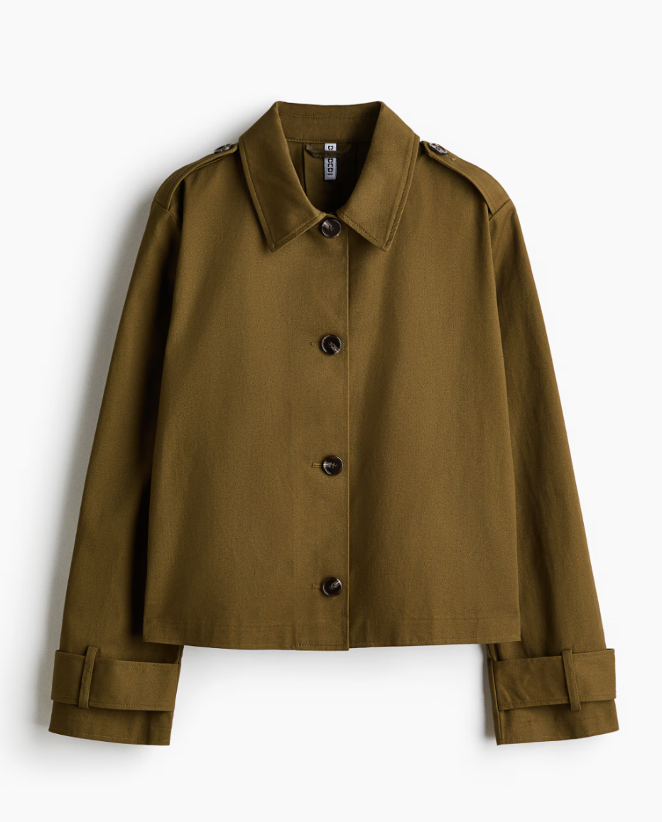 An olive green, cropped cotton trench-style jacket from H&M featuring a structured collar, black buttons, and military-inspired shoulder epaulettes."