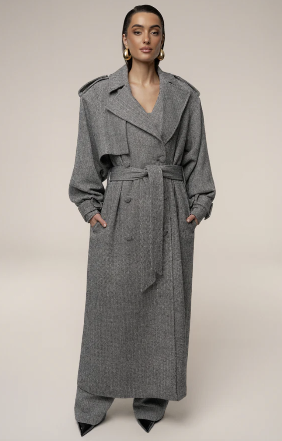 A full-length view of the JLuxLabel Herringbone Oversized Trench Coat, a textured grey long coat with a belted waist and structured shoulders, styled as part of a fashion editor-inspired outfit.