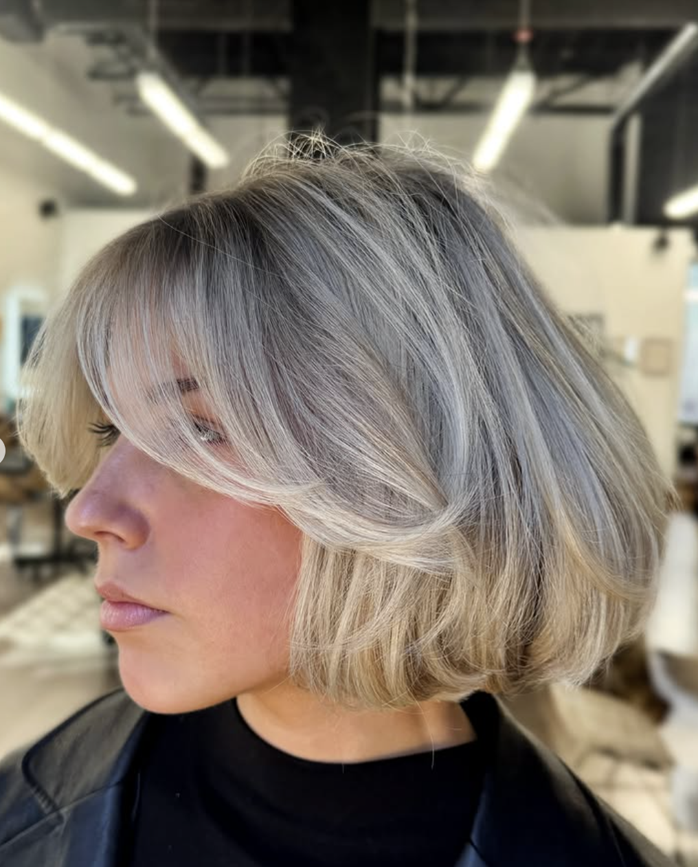 A woman over 50 with a modern chin-length layered bob featuring feathered silver-blonde curtain bangs.