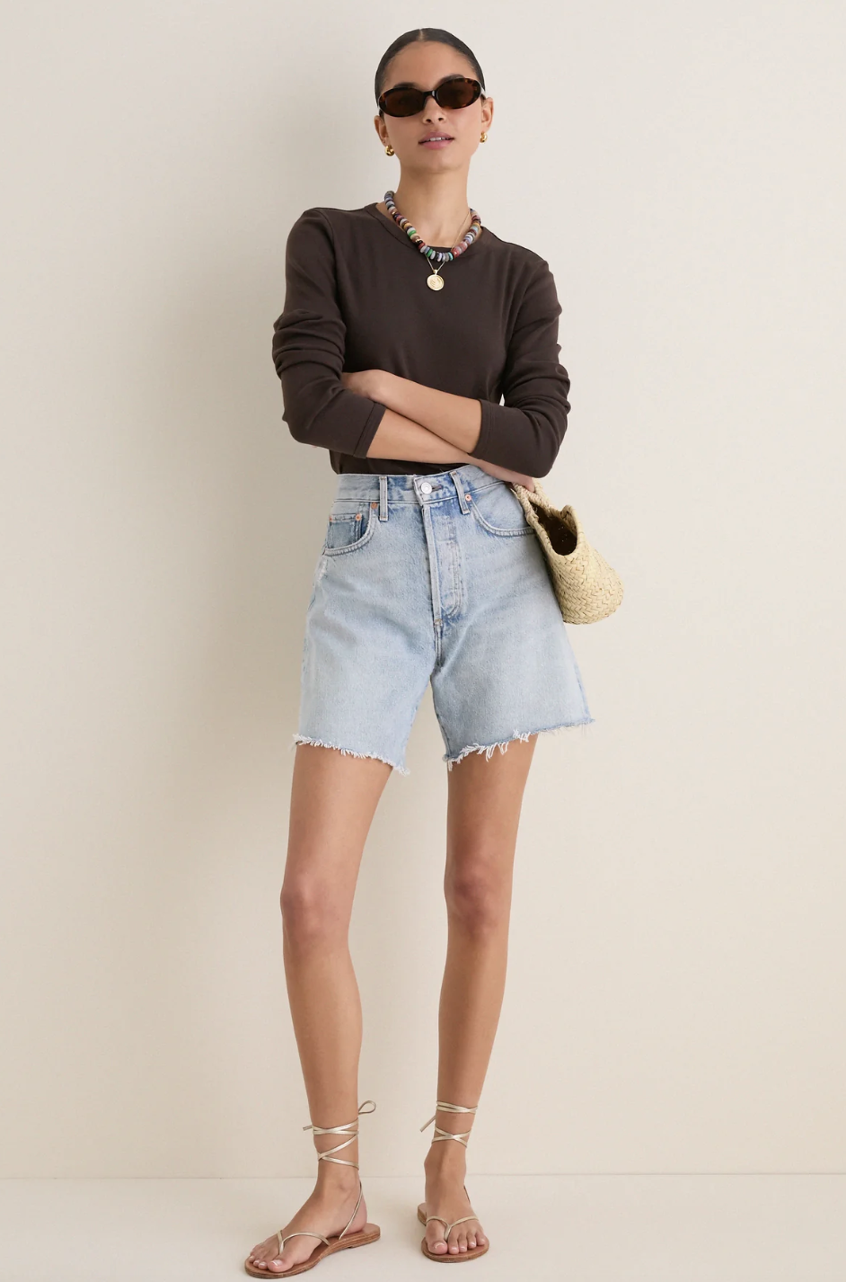 Model wearing an espresso brown long-sleeve knit top styled with light-wash denim shorts and lace-up sandals on a white background.