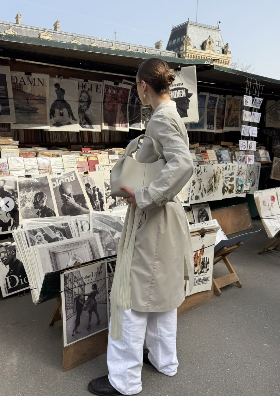 A close-up of a woman wearing a wide black leather belt with long fringe tassels layered over a grey blazer and matching trousers.