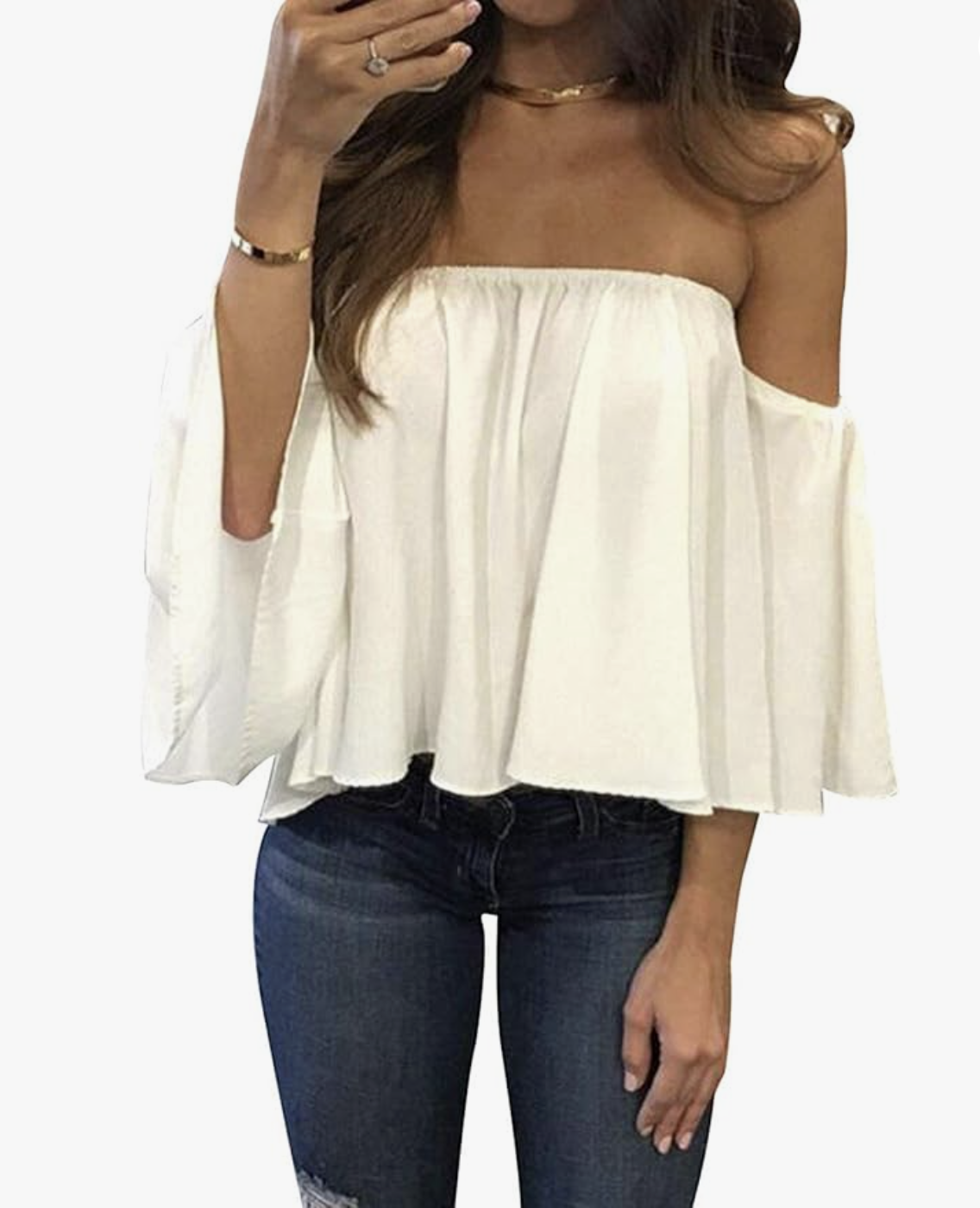A woman wearing a white off-shoulder poplin top with flared sleeves, styled with dark wash denim jeans and gold jewelry.
