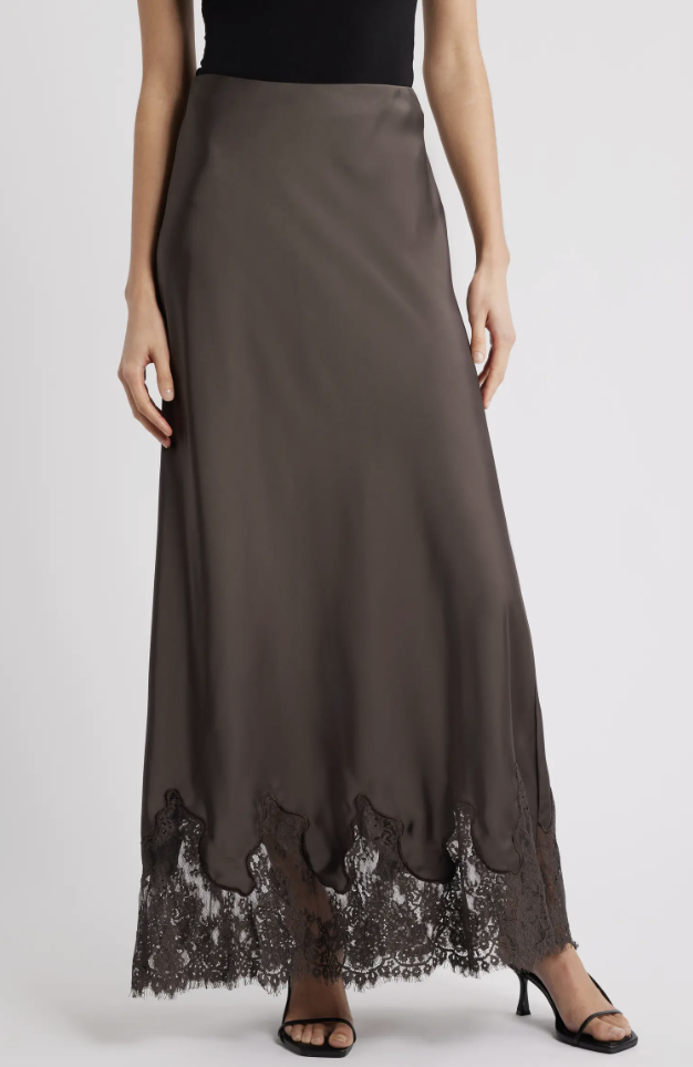 A woman wearing a charcoal grey satin bias-cut midi skirt with black lace trim along the hem, styled with black strappy heels.