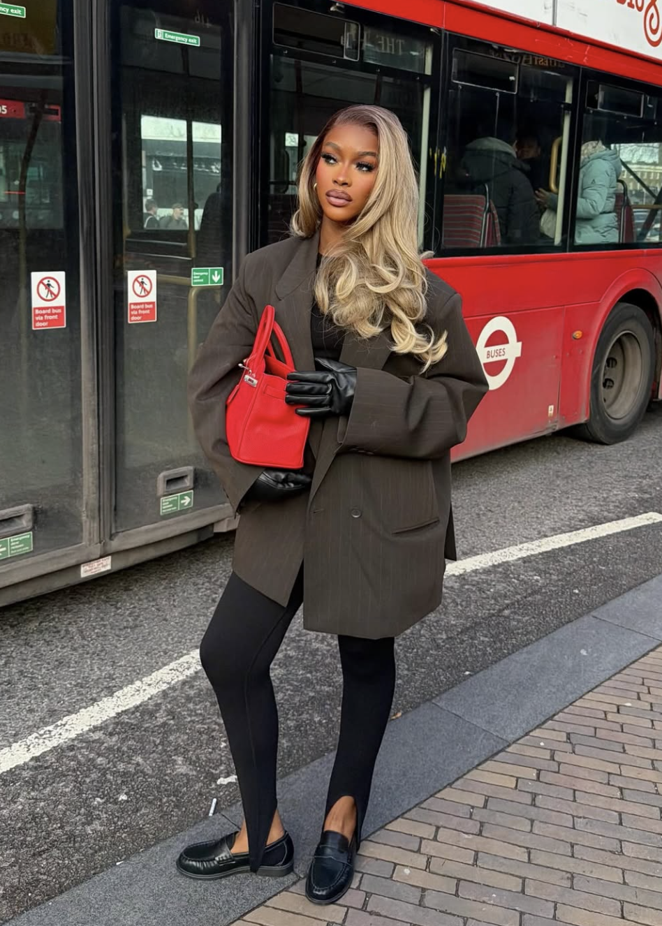 Woman wearing black stirrup leggings with an oversized dark brown blazer, black leather loafers, and a pop-of-color red handbag.