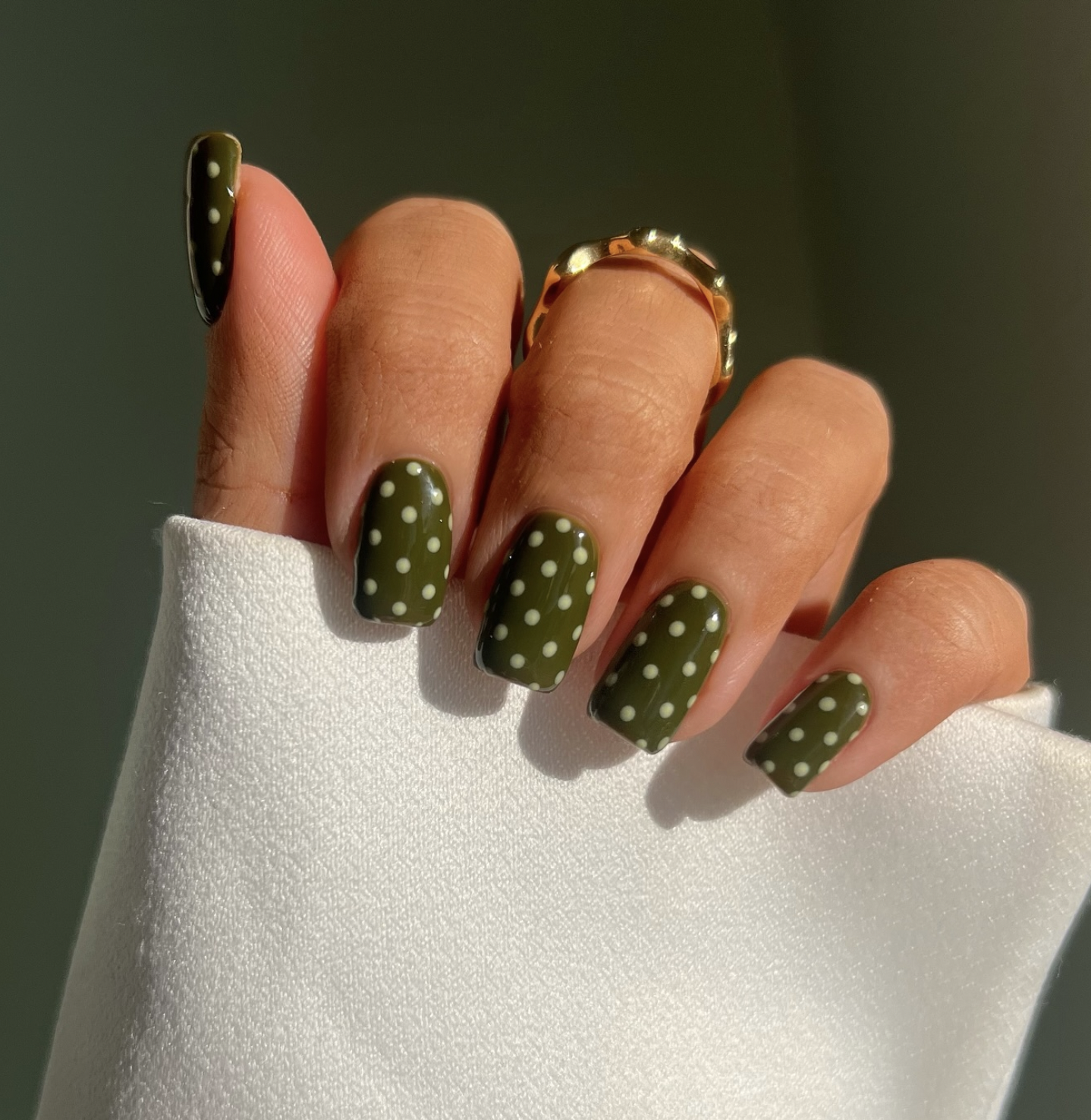 Short squoval nails painted glossy olive green on a Black woman's hand