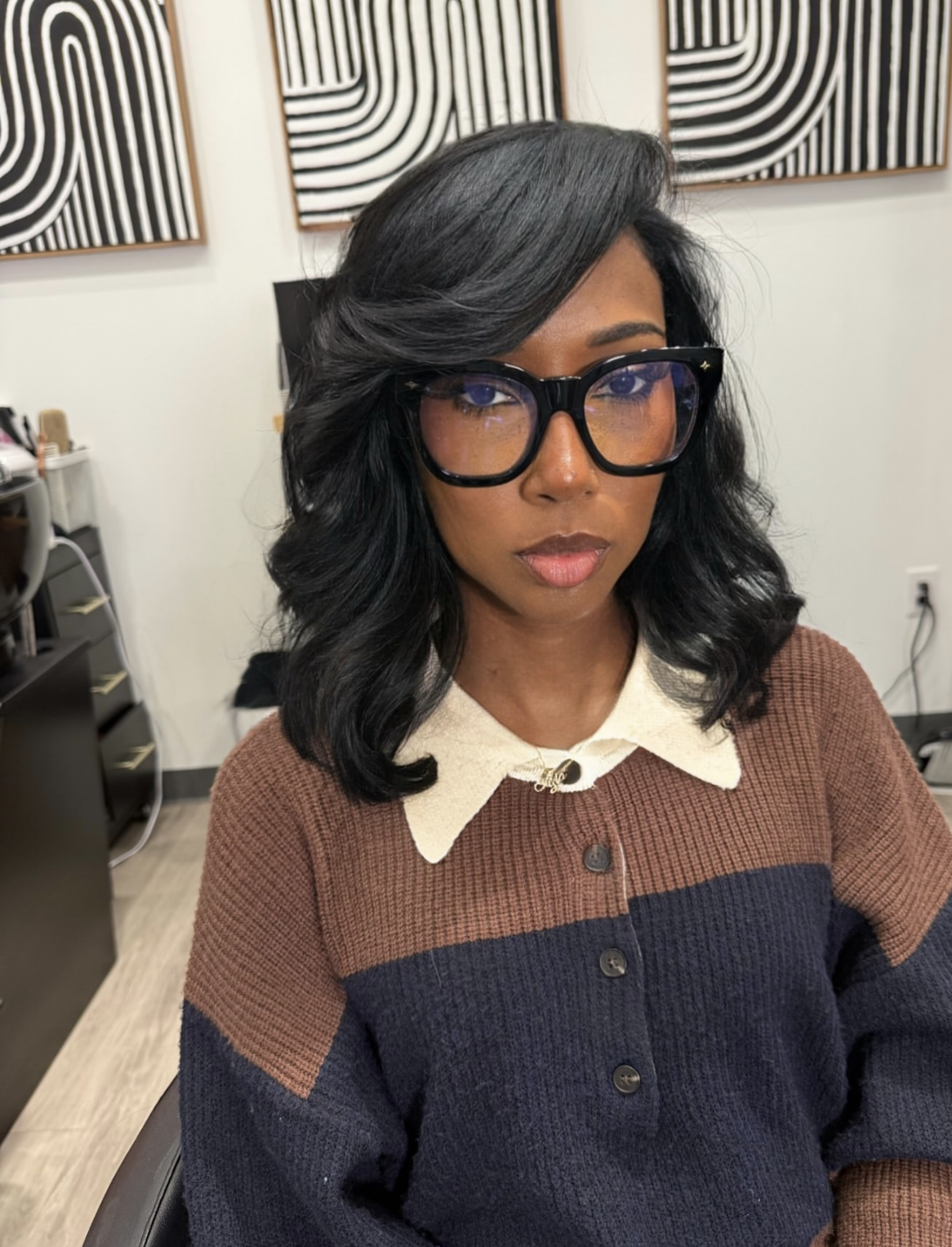 A woman with glasses and dark, medium-length hair styled in a bouncy butterfly haircut with side-swept layers.