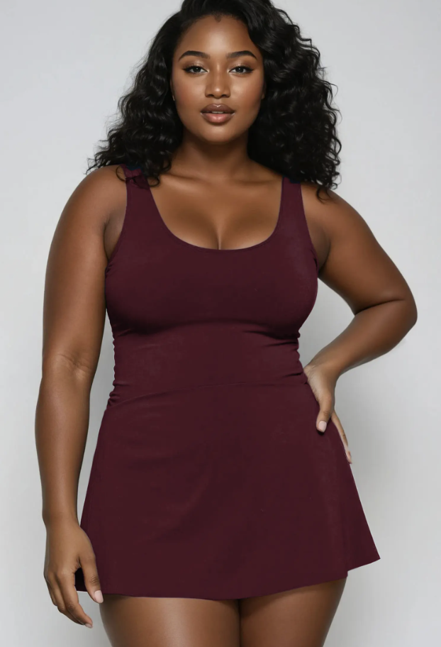 A maroon tankini-style swim dress with thick, supportive shoulder straps and an A-line silhouette, shown on a plus-size model as a versatile vacation wardrobe option.