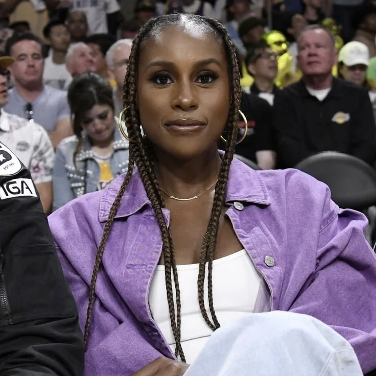 Issa Rae wearing a purple denim jacket, featuring long knotless braids with a sharp middle part to demonstrate how vertical lines elongate a round face shape.