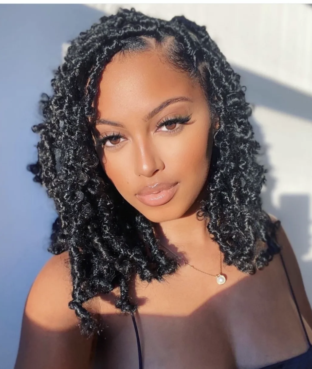 A woman with an oval face shape wearing mid-length butterfly locs with a distressed, curly texture and a side part.