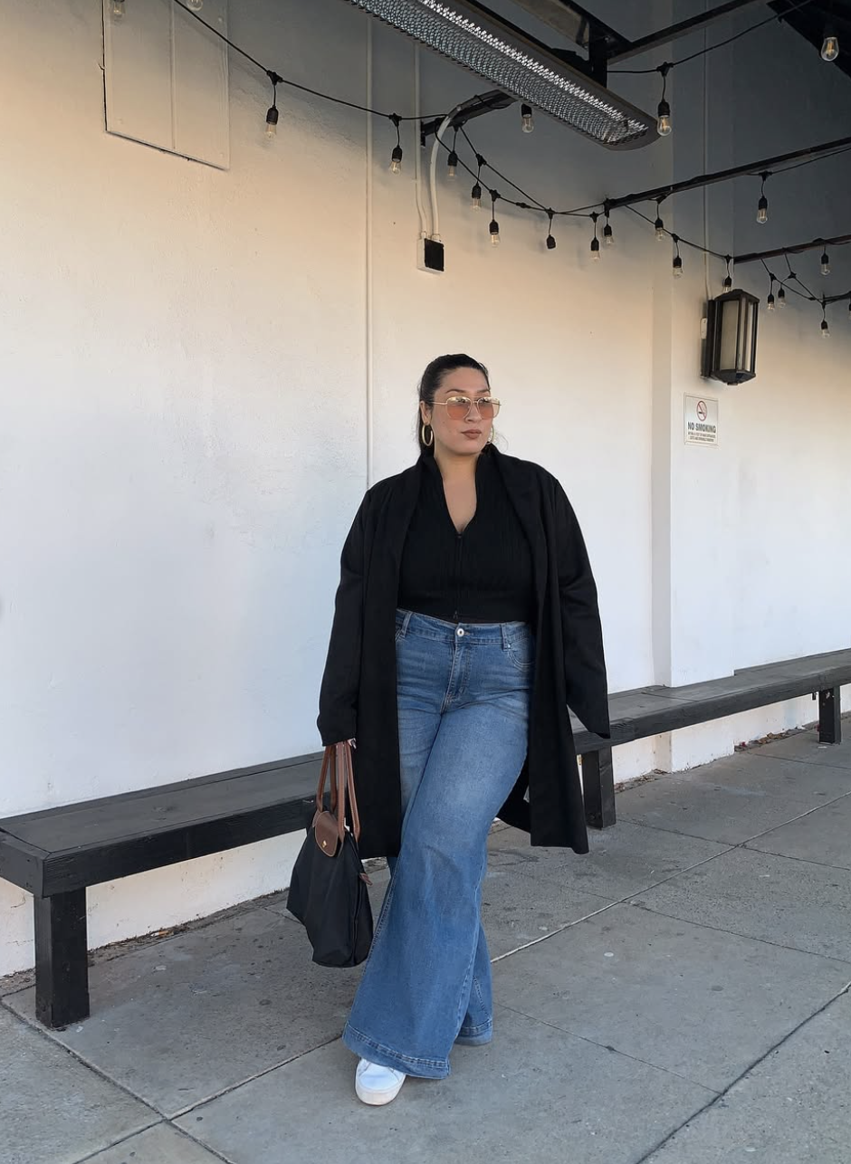 A fashion editor-inspired casual look featuring light-wash wide-leg jeans paired with chunky white sneakers and a long black coat, styled by @cidscloset.
