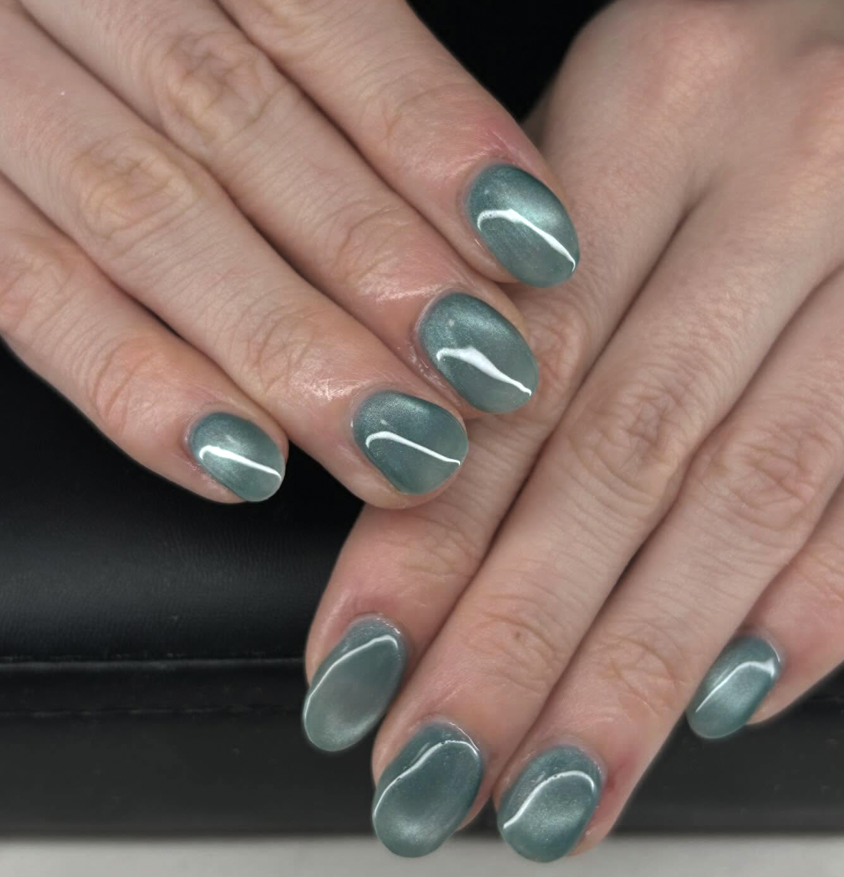 A close-up of glossy, medium-length round nails featuring a magnetic sea glass green cat-eye polish with a luminous silver velvet shimmer, showcasing cute June nail ideas.