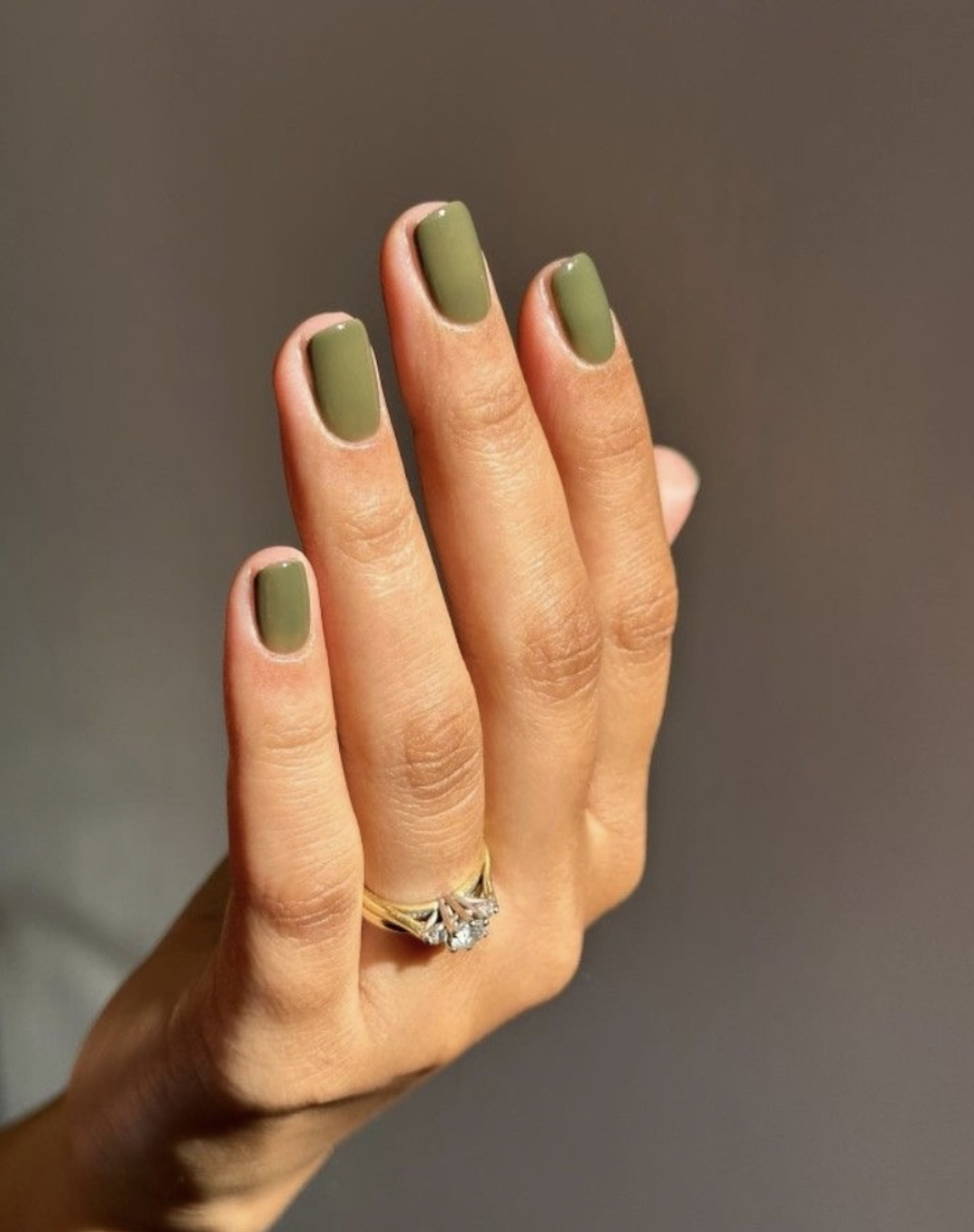 Close-up of almond-shaped nails painted in a solid, high-shine olive green polish.