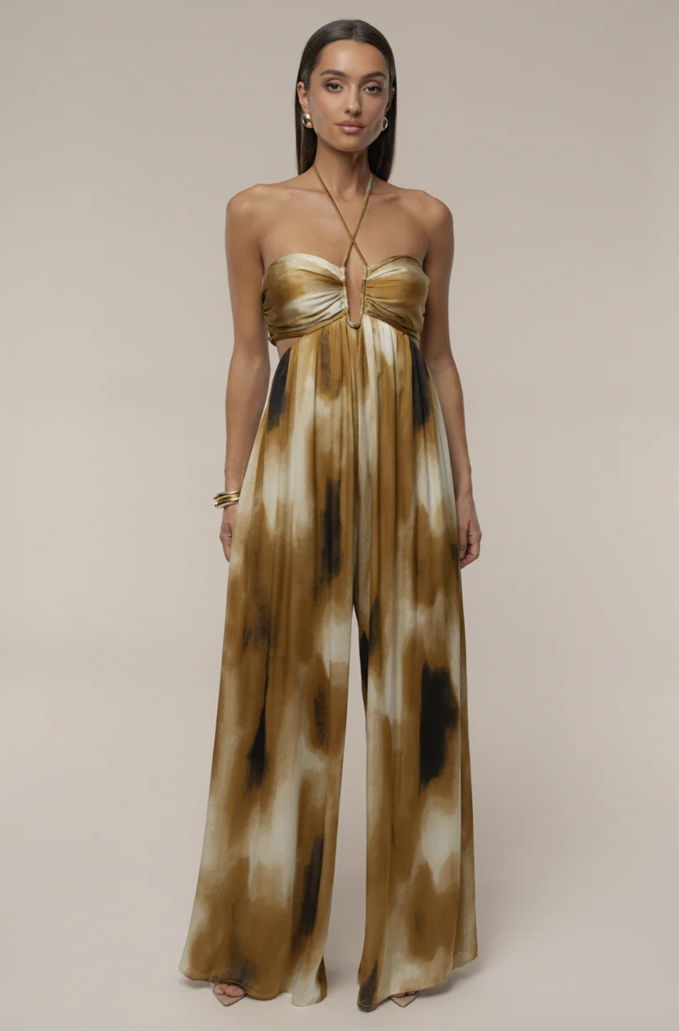 A woman wearing the JLUXLABEL Gold Safari Sunset Jumpsuit with an abstract gold and tan watercolor print, sweetheart neckline, and center waist cutout.