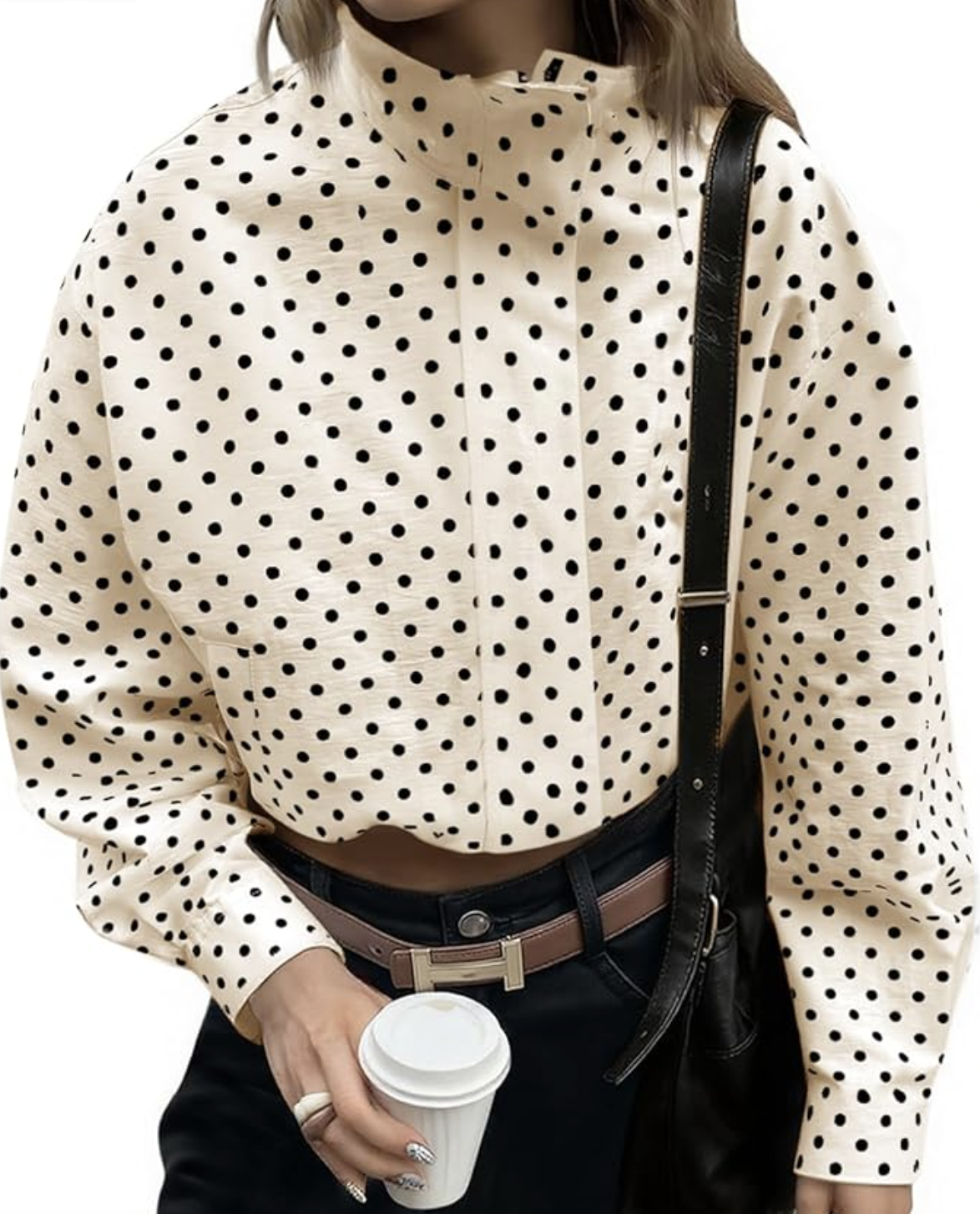 A close-up of a white oversized button-down jacket with large black polka dots, styled with a thin brown leather belt and black trousers.