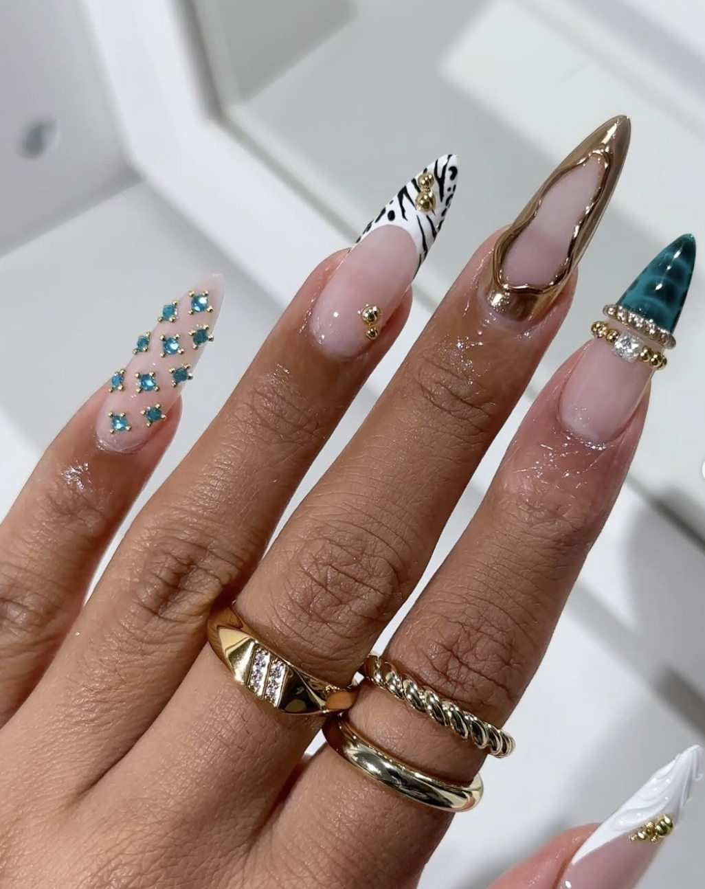 Long almond nails with zebra print tips and 3D gold chrome bangle accents.