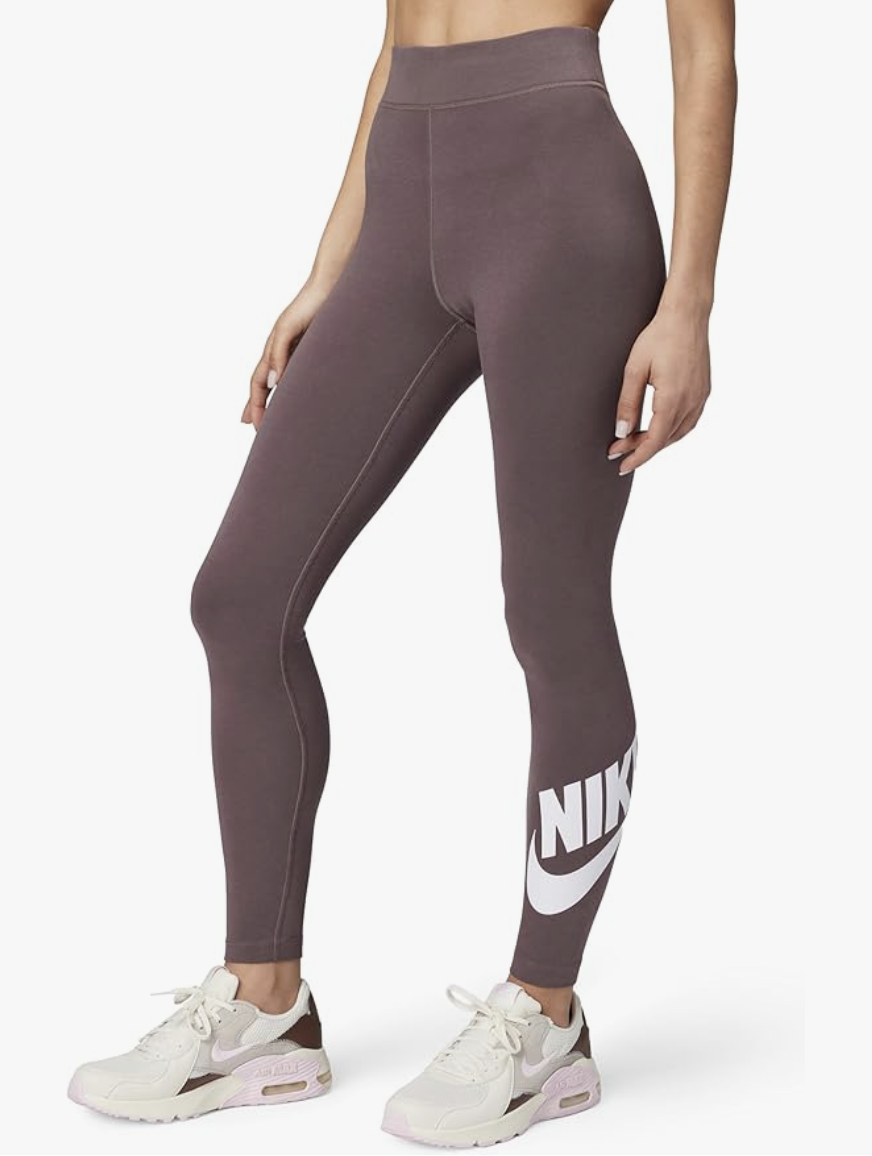 A woman wearing the Nike Sportswear Classics High-Waisted Graphic Leggings in the color Tattoo, featuring a large white Nike logo on the lower leg.