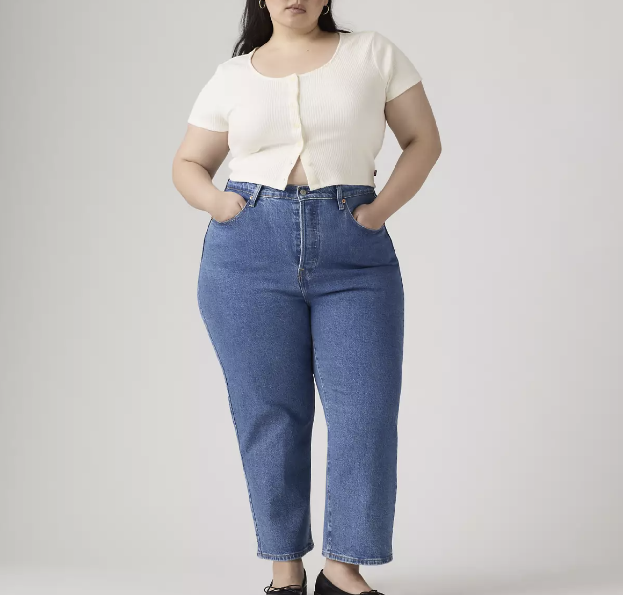 A curvy woman wearing medium-washpaired with a white short-sleeve button-down shirt. These ultra high-rise jeans are designed to hit above the belly button for a secure and flattering fit.