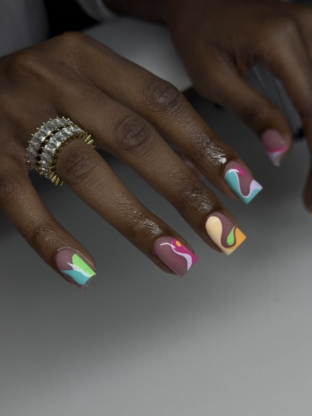 A close-up of short nails featuring colorful pastel abstract shapes, swirls, and color blocking over a natural nude base.