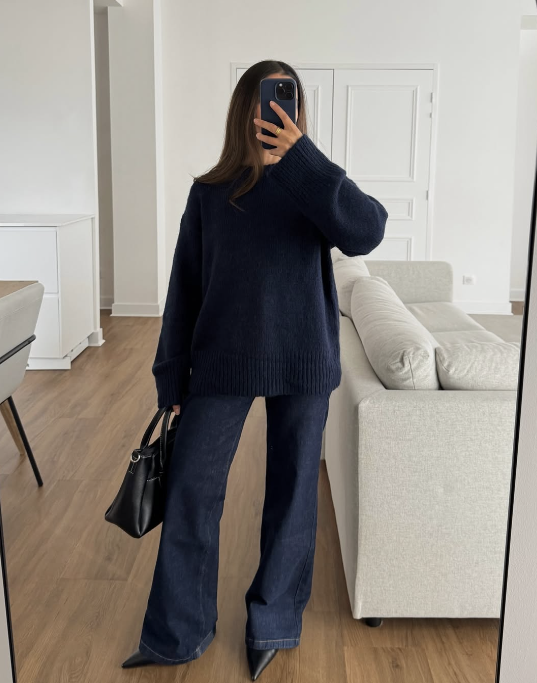A woman wearing an oversized navy blue chunky knit sweater with matching dark blue jeans and a black handbag, styled for a cozy and monochromatic everyday look.