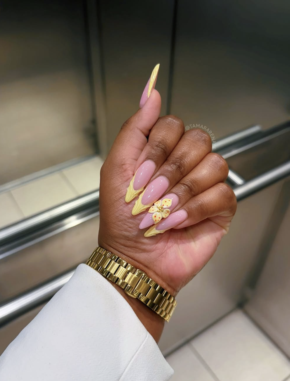 Long, almond-shaped nails with a sheer pink base coat, featuring a pale yellow French tip upgraded with a textured, 3D yellow-and-white floral accent design.