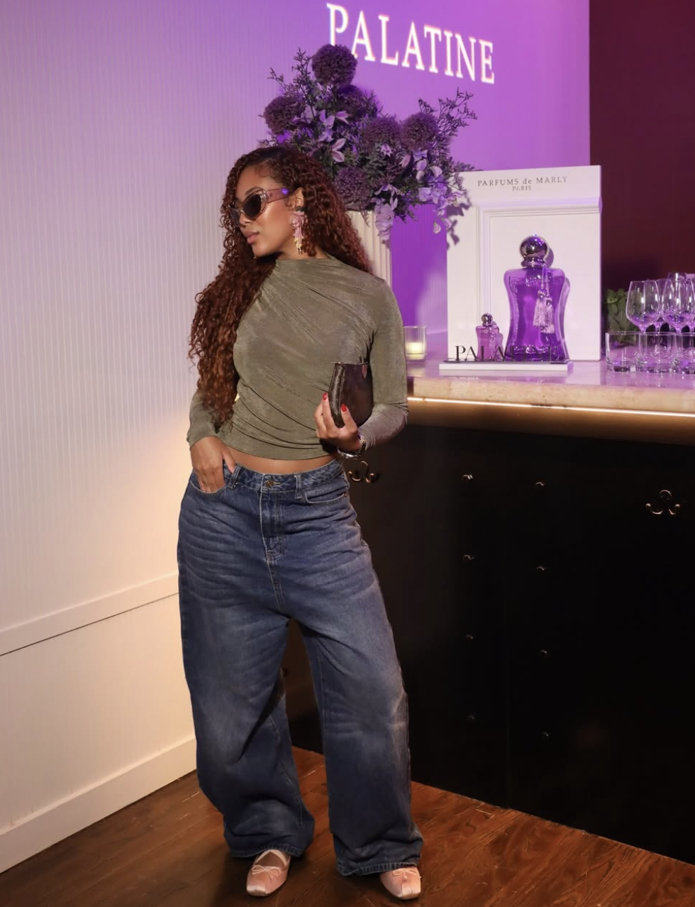 A woman wearing dark-wash baggy jeans with a brown satin long-sleeve top and pink ballet flats to demonstrate a dressy evening outfit formula.