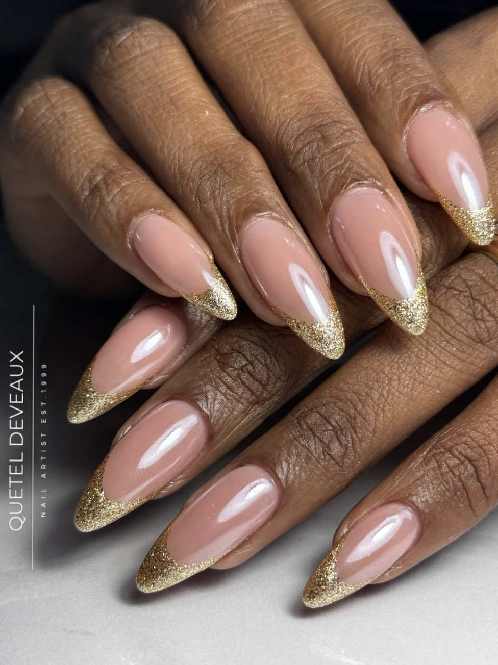 Long, almond-shaped nails featuring a semi-sheer nude base coat with a high-shine pearl chrome glaze, accented by delicate gold leaf flakes along the tips.