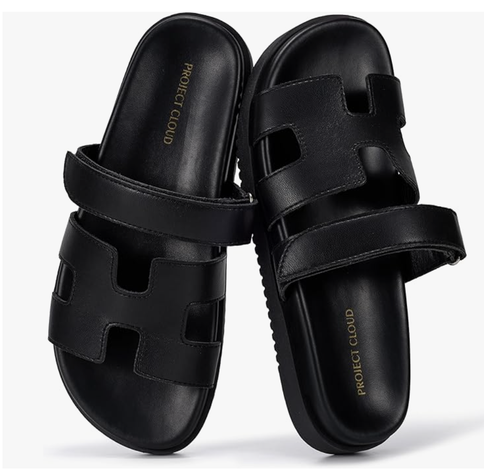 A pair of minimalist black H-band slide sandals with a cushioned sole, styled as a versatile footwear option for a Mediterranean resort vacation.