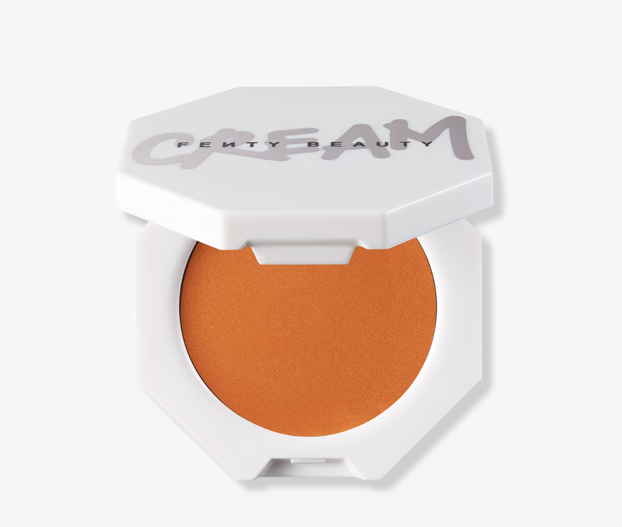 An open white hexagonal compact of Fenty Beauty Cheeks Out Freestyle Cream Blush in the shade Fuego Flush, showing a vibrant tangerine-orange cream with a subtle gold shimmer.