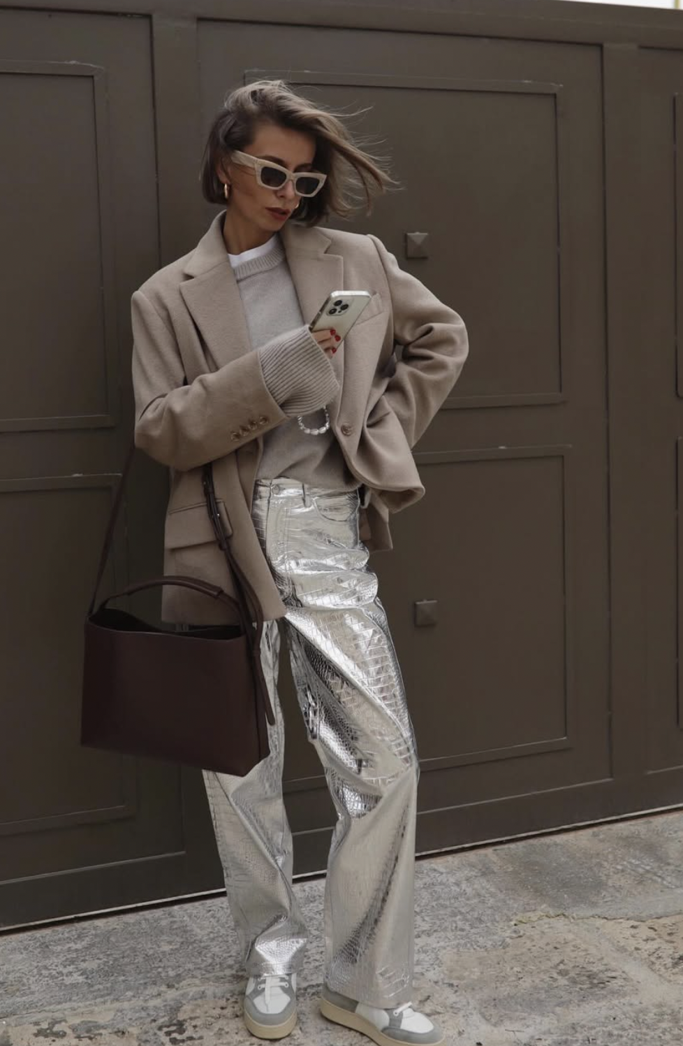 Woman wearing silver metallic leather pants with an oatmeal blazer, gray sweater and sneakers