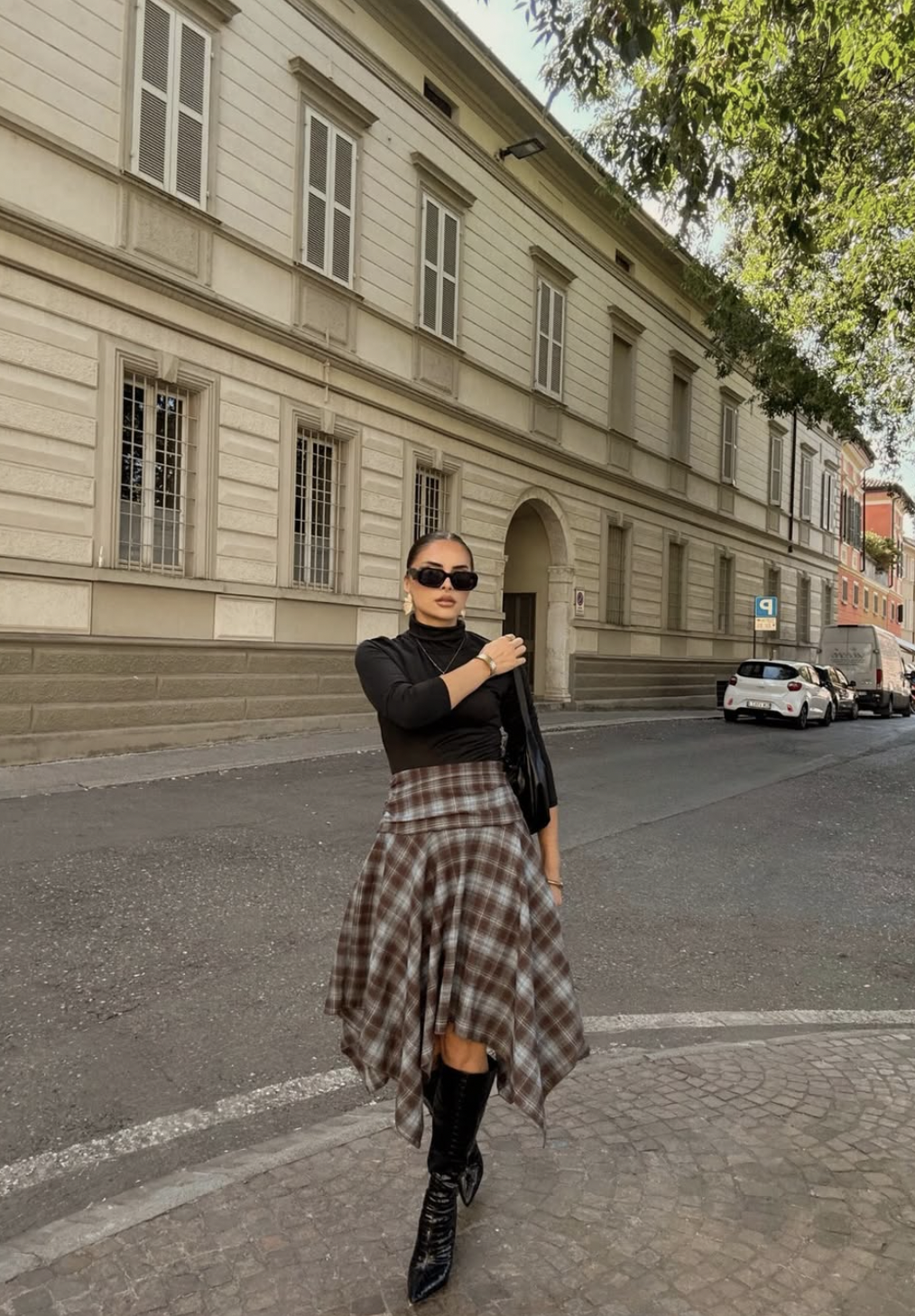 Woman wearing a plaid handkerchief-hem midi skirt with a black turtleneck and slouchy knee-high boots