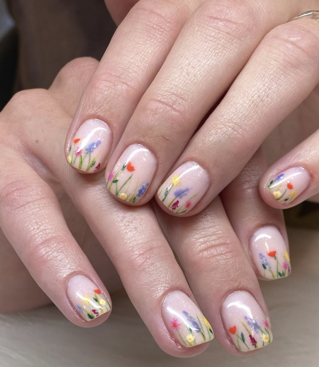 Short natural nails with a sheer base featuring tiny, colorful hand-painted wildflowers in red, blue, and yellow.