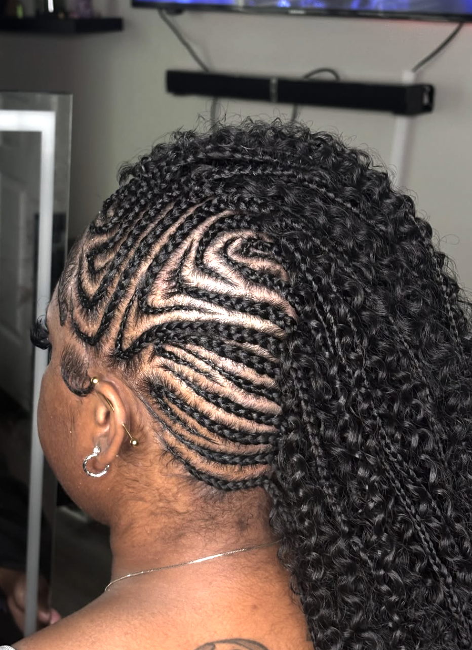 A close-up side profile of a woman with an intricate braided faux hawk featuring curved cornrow patterns on the sides and a voluminous braided center, highlighting a sharp diamond face shape.