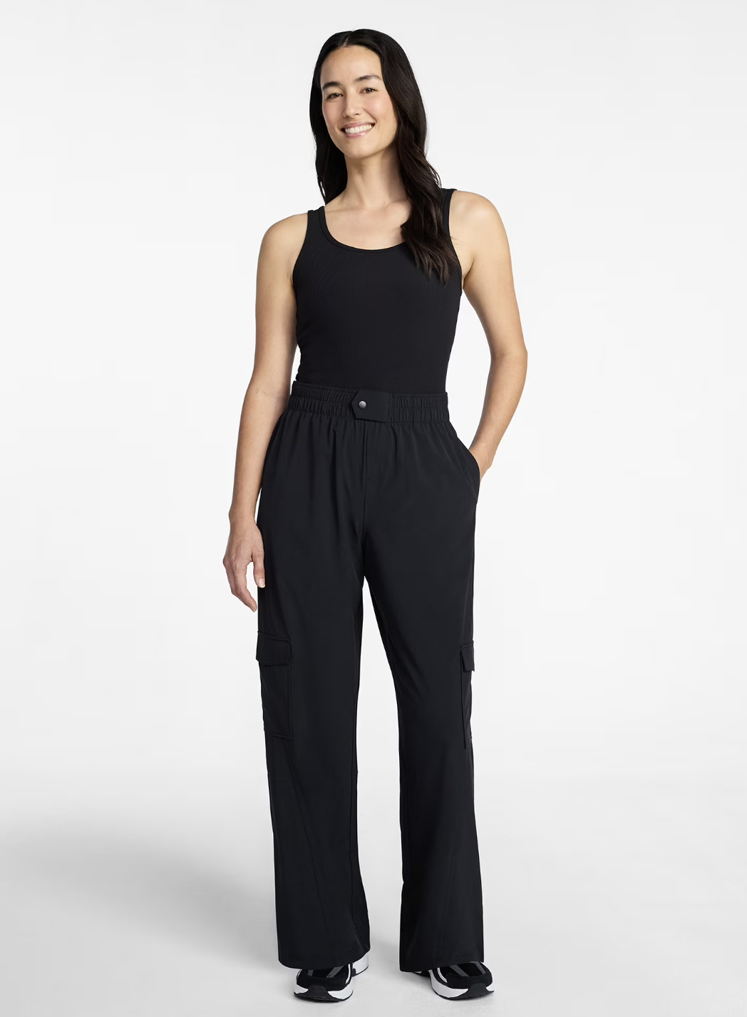 A person wearing a black sleeveless cargo jumpsuit with wide-leg trousers and utility pockets, styled with black and white sneakers for a modern, utilitarian-inspired outfit.