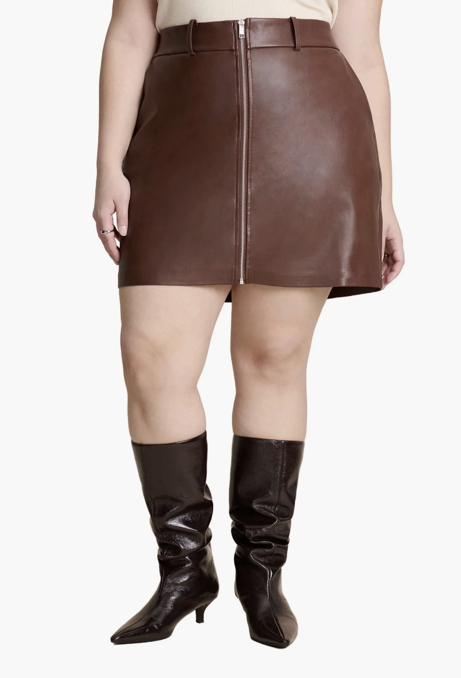 A brown faux leather mini skirt with a side slit and belt loops, styled with black knee-high slouchy boots, ideal for pairing with flats for women for a balanced look.