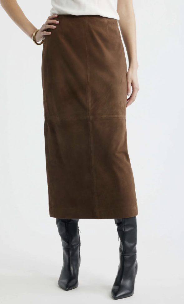 A model wearing a brown suede midi skirt paired with black pointed leather knee-high boots.