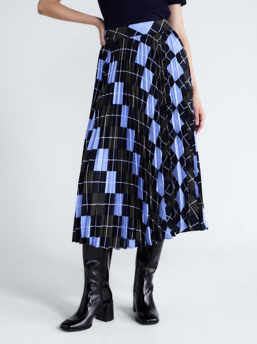 Woman wearing a blue and black plaid pleated midi skirt with a navy top and black patent knee-high boots.