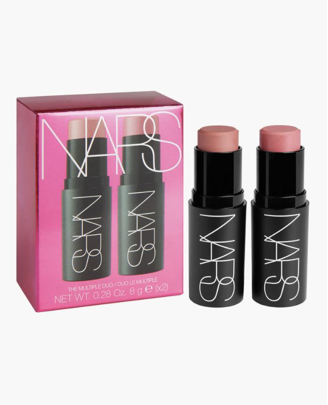A close-up of the NARS The Multiple Stick Duo in a metallic pink box, showing two cream makeup sticks in neutral and blush shades.
