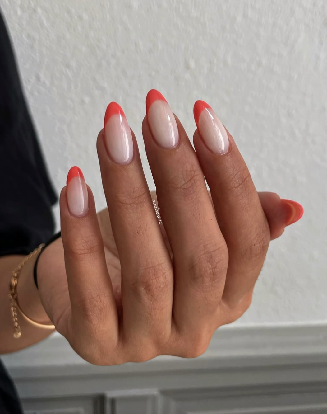 A close-up of long, almond-shaped nails featuring a bright neon coral French manicure, showcasing flawless precision on the curved tips.