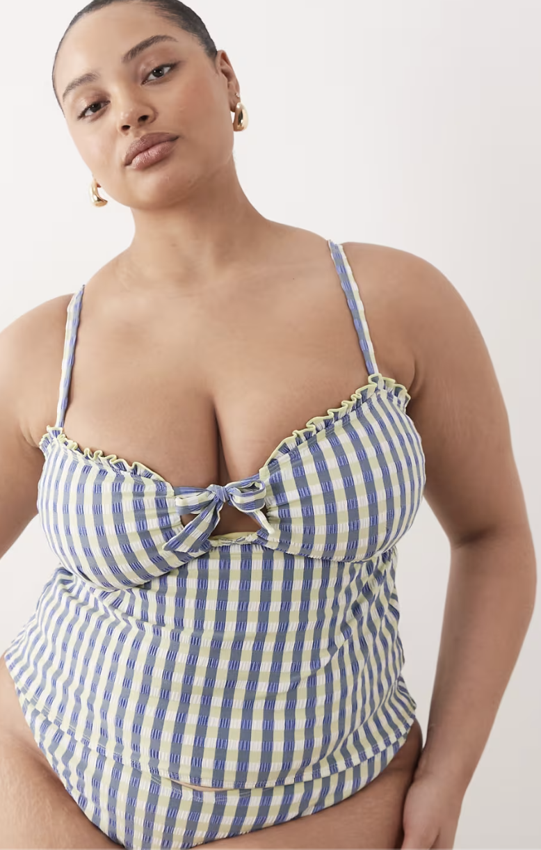 A woman wearing a blue and white gingham tiered tankini top with ruffle straps and a bow detail, part of the best tankinis for a classic 2026 summer look.