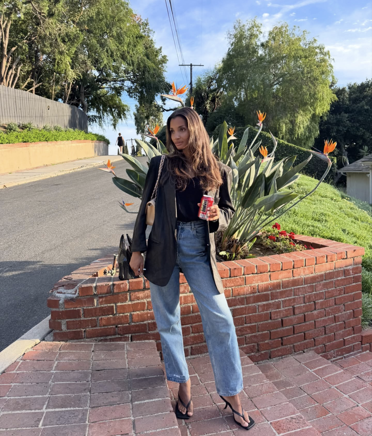 Woman wearing a black blazer, white tank top, light wash cigarette jeans, and heels.