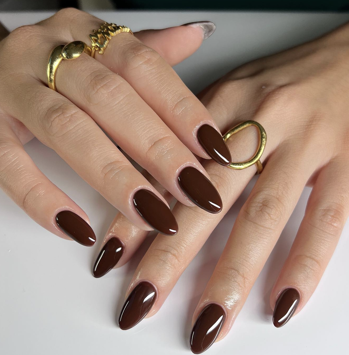 Glossy chocolate brown polish on almond-shaped nails.