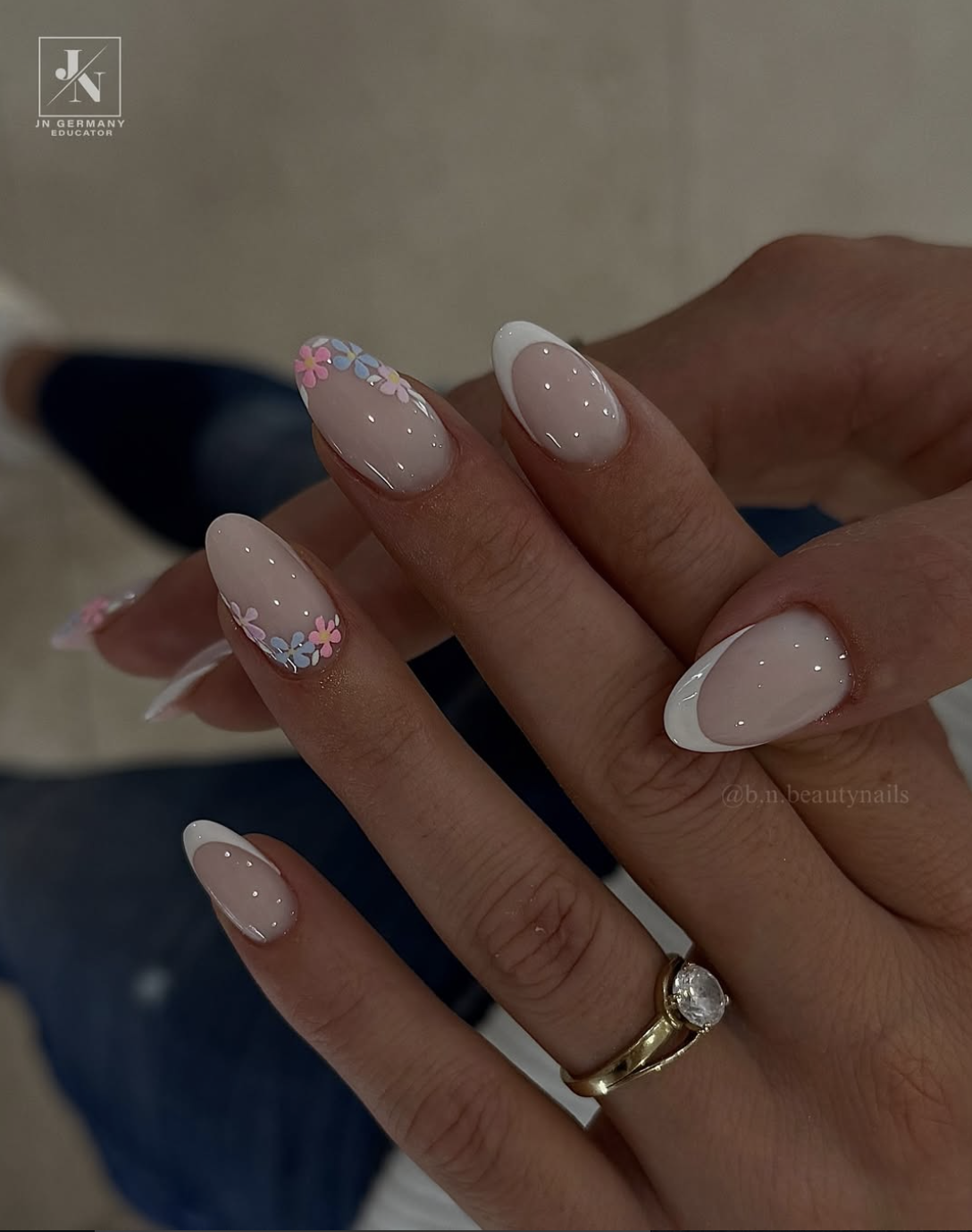 Almond-shaped nude nails with delicate, hand-painted white micro-flowers along the edges.