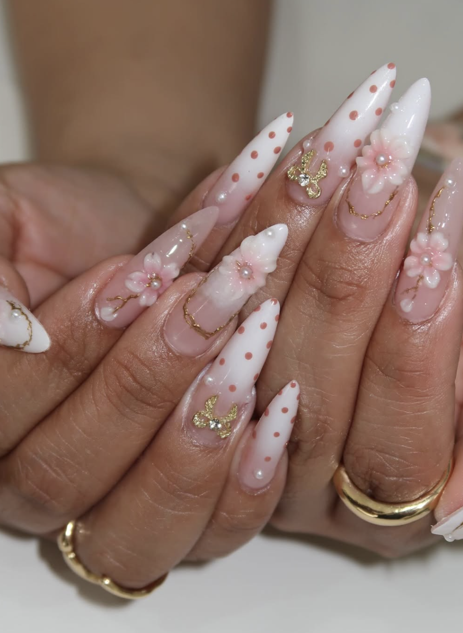 Long almond-shaped nails with a sheer base, featuring hand-painted pink cherry blossom flowers, delicate 3D floral petals, and gold wire accents with tiny pearl centers.